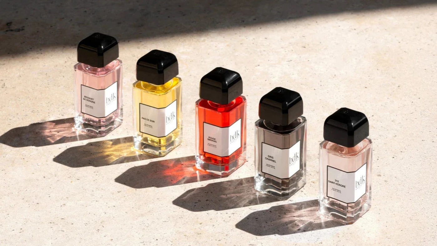 Five small perfume bottles with black caps on a textured surface. BDK perfumes